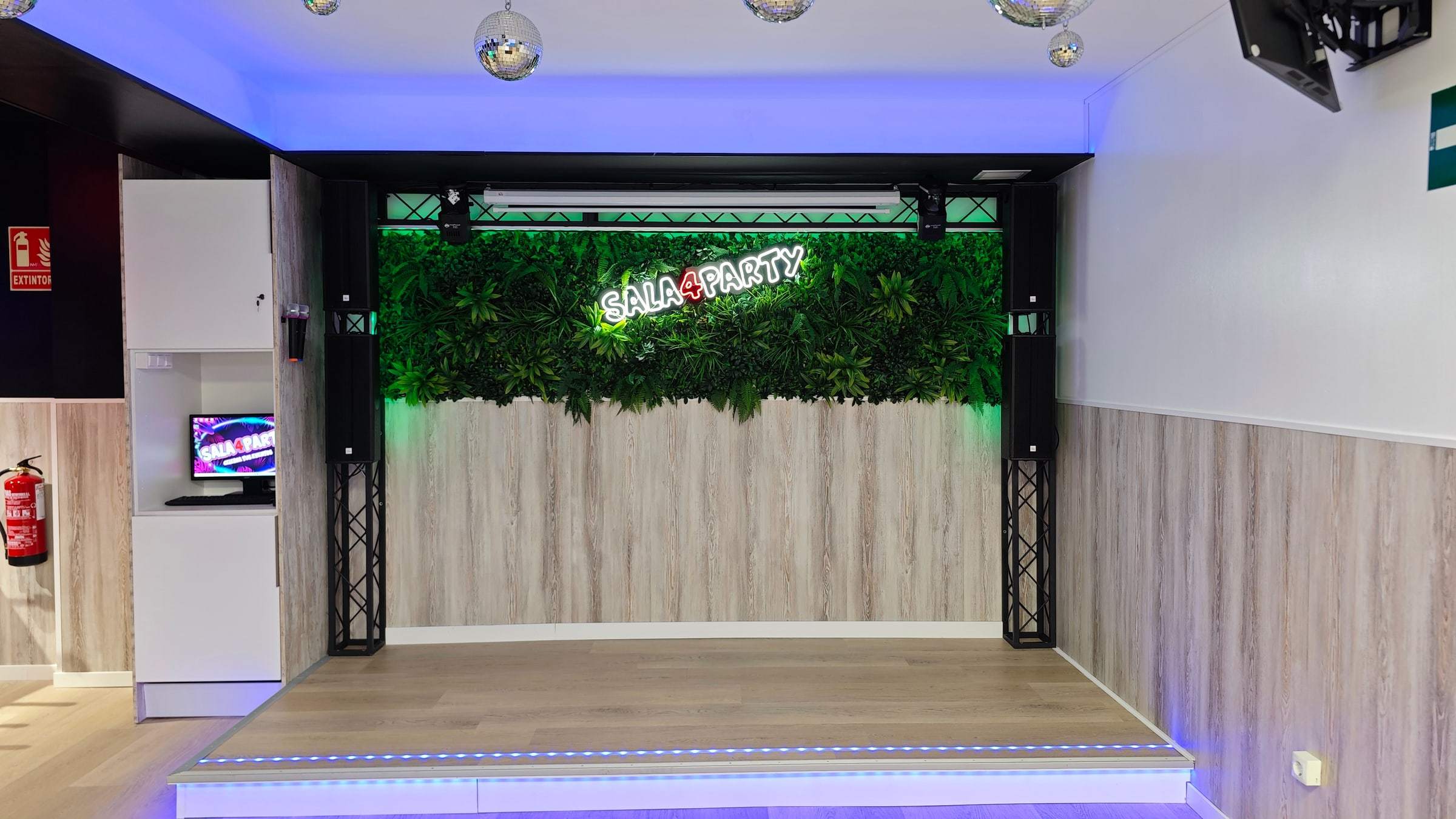 Escenario con pared vegetal, focos y el letrero de neón de Sala4Party