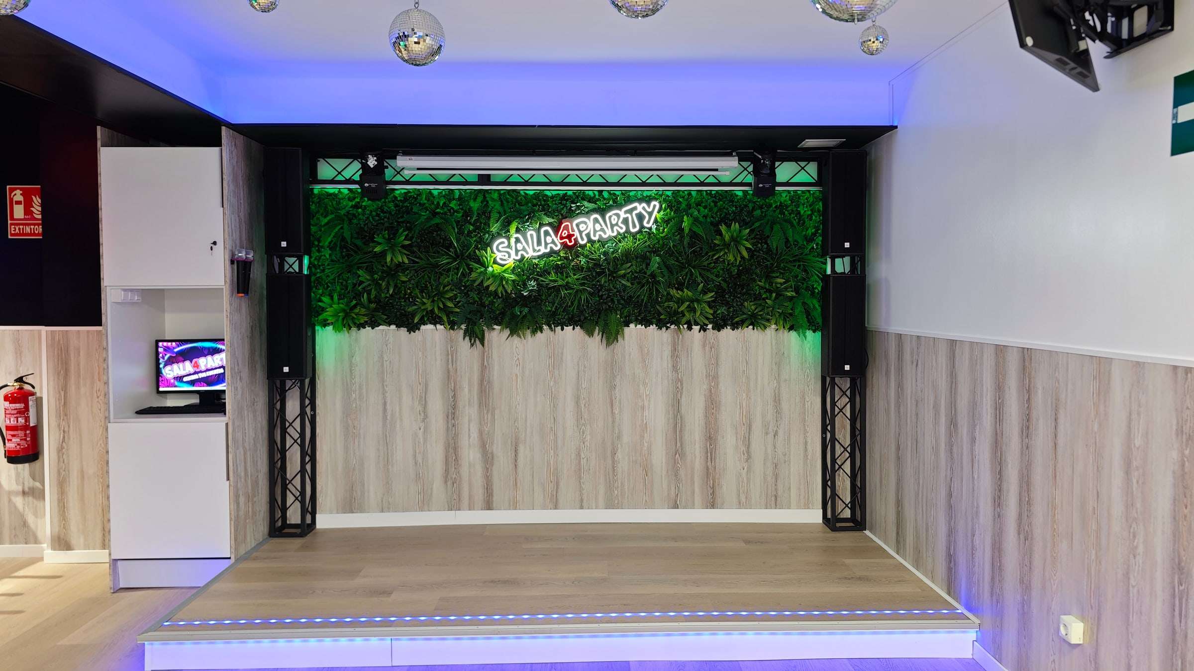 Escenario con pared vegetal, focos y el letrero de neón de Sala4Party
