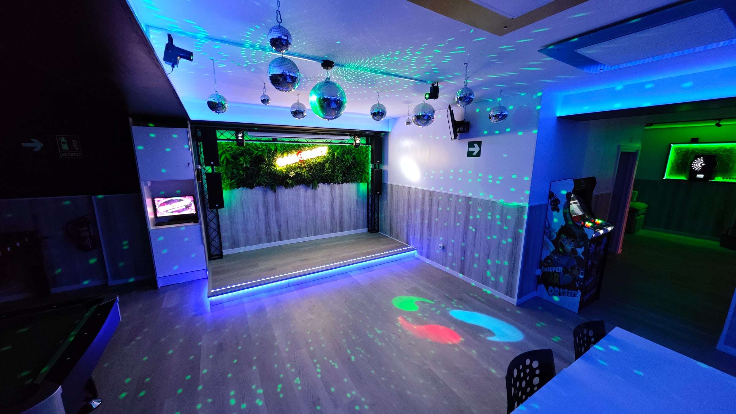 La sala con luces de fiesta, el escenario al fondo y una máquina recreativa a la derecha