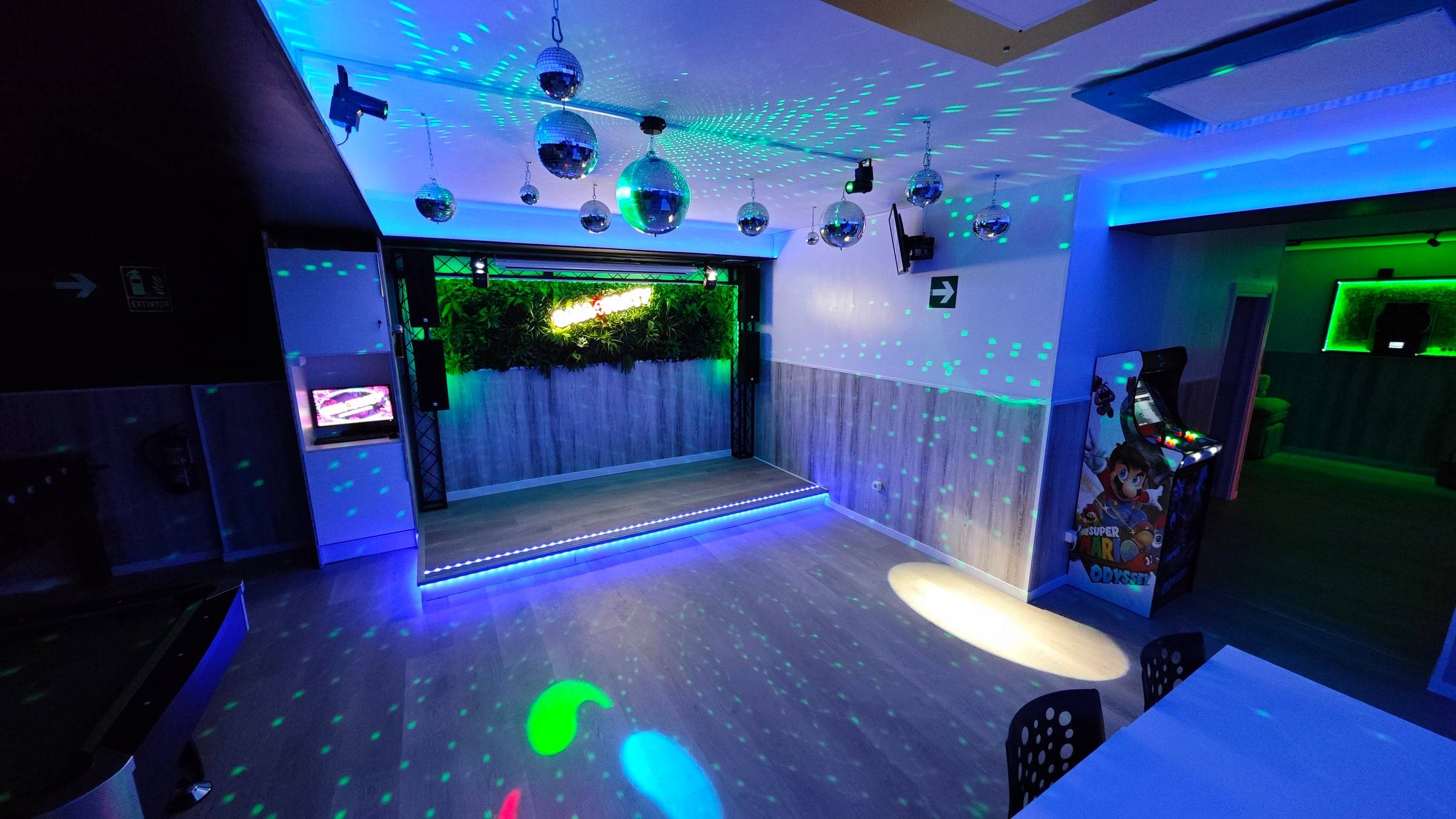 Sala4Party con la iluminación de discoteca encendida: escenario con pared vegetal, bolas de espejo y luces de colores